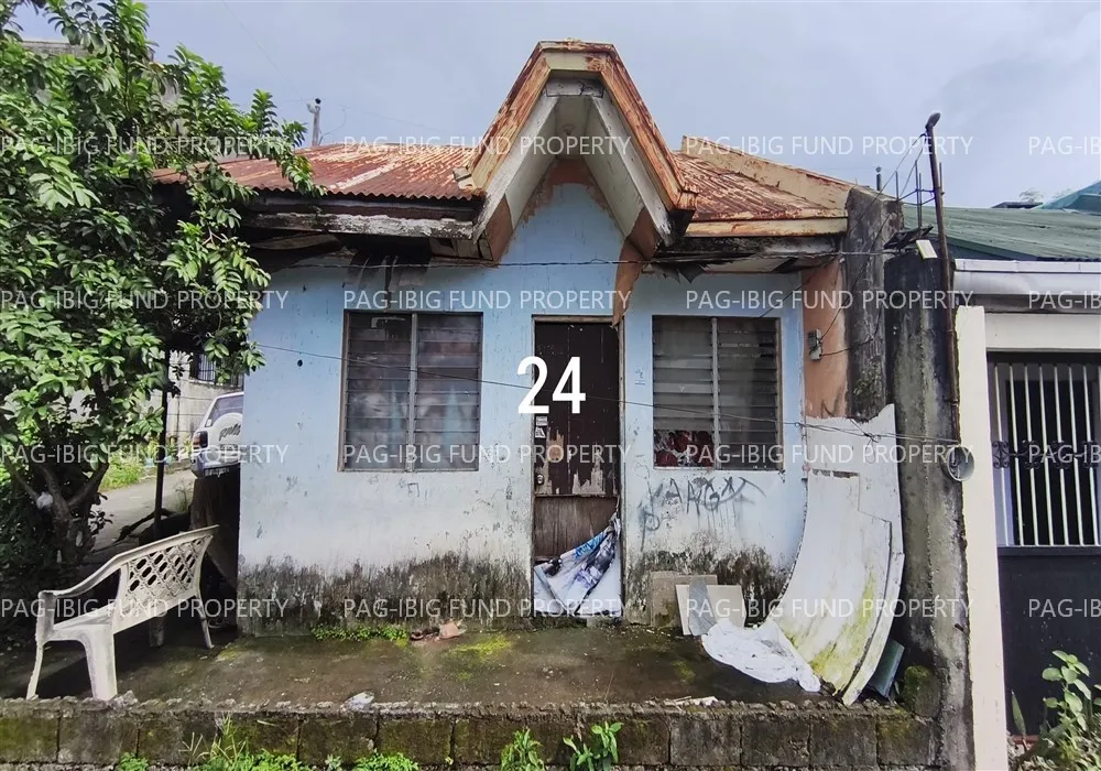 Front of the single-storey single-attached house in Kingstown Subdivision, Caloocan, with a pale blue weathered facade, a gabled entrance and louvered windows, photographed for the Pag-IBIG auction listing