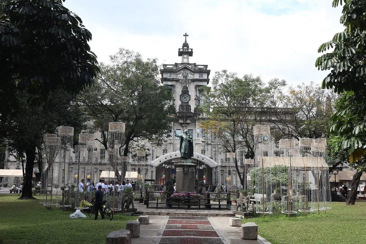 University of Santo Tomas Main Building in Sampaloc, Manila, with uniformed students gathered near the monument